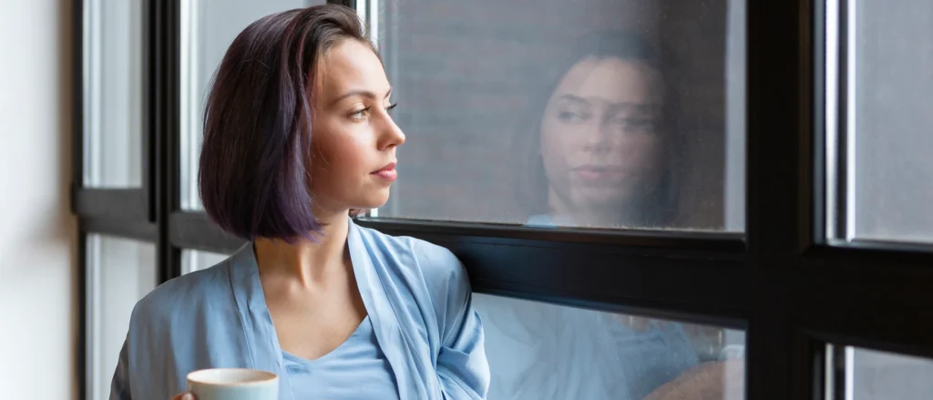 Nachdenkliche Frau mit Kaffeetasse blickt aus dem Fenster